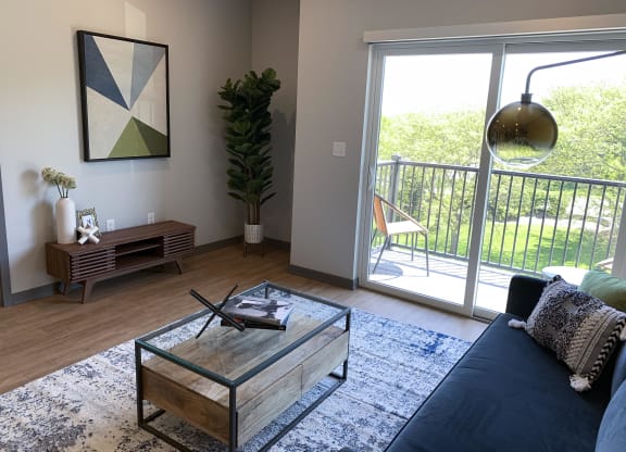 Spacious furnished living room with hard wood style flooring and scenic view of tree line in Lincoln at Haven at Uptown.
