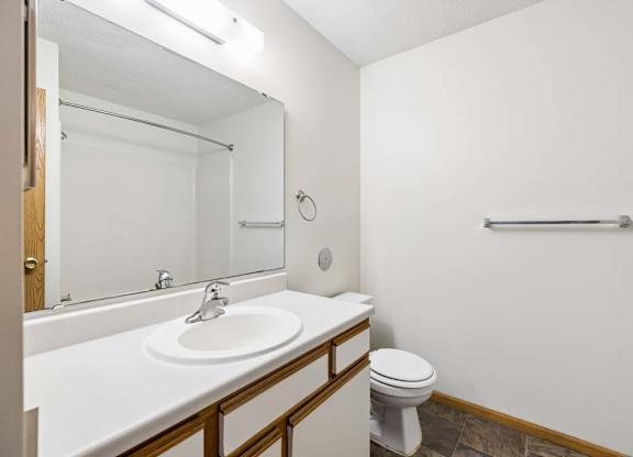 Apartment bathroom with a single-sink vanity, white and wood-tone cabinetry, a large mirror with overhead lighting, and a tub-shower combination with a towel bar.