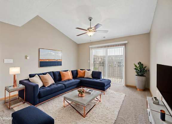 Virtually staged living room with a sectional sofa, coffee table, ceiling fan, large window, and neutral apartment finishes.