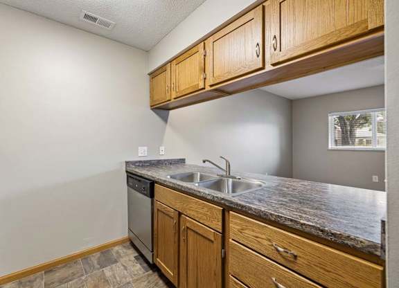 Apartment kitchen with wood cabinetry, black appliances, a double-basin sink, laminate countertops, and a pass-through opening connecting to the living area.