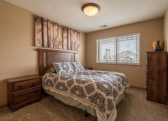 a bedroom with a large window for natural light, with a queen bed and wooden furniture.