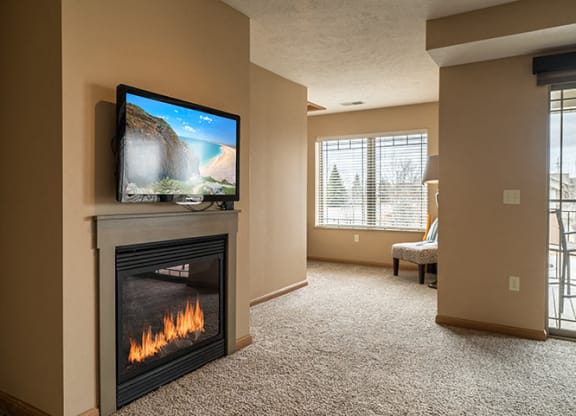 a living room with a gas fireplace with a tv mounted above it, next to a den space