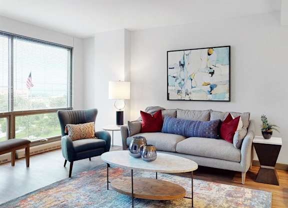 A living room with a grey couch, a black chair, a wooden coffee table, and large windows