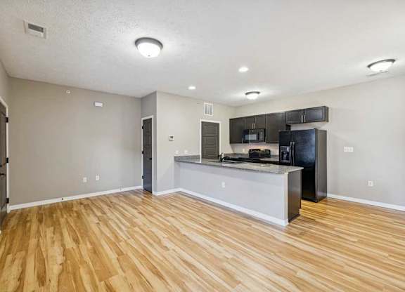 An apartment kitchen with wooden floors, black appliances, and granite countertops..