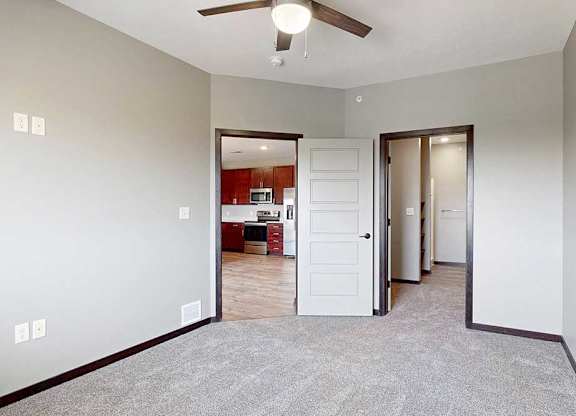 A carpeted bedroom with a ceiling fan and a walk-in closet and attached bathroom.