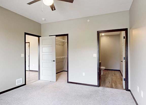 A carpeted bedroom with a ceiling fan, a walk-in closet, and an attached bathroom.
