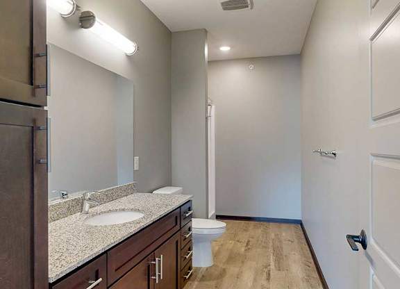 A long bathroom with a granite vanity sink, mirror, tall cabinet, and walk-in shower..