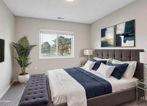 Virtually staged bright apartment bedroom with large window, neutral walls, upholstered bed, and modern furnishings with soft natural light.