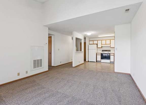 A spacious living room with a grey carpet and white walls.
