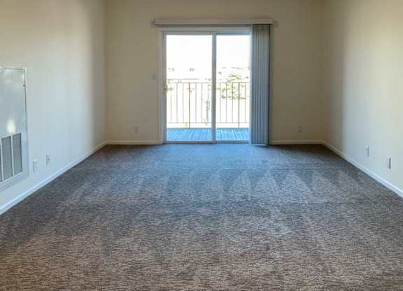 a living room with carpeted flooring and a sliding glass door to a balcony