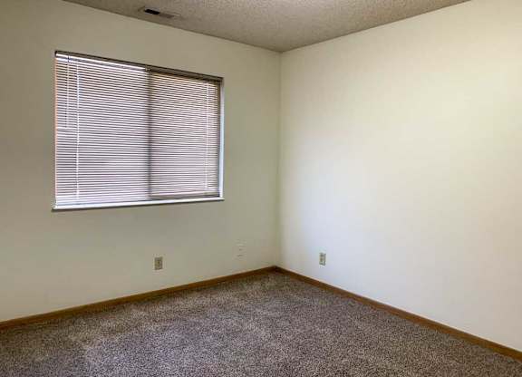 a bedroom with white walls, carpeted flooring, and a window with blinds