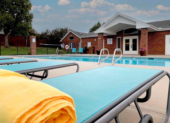 apartment swimming pool with two light blue lounge chairs a clubhouse in the background
