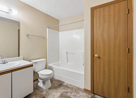 Apartment bathroom with a single-sink vanity, large mirror, toilet, tub/shower combination, and durable flooring with neutral finishes throughout.