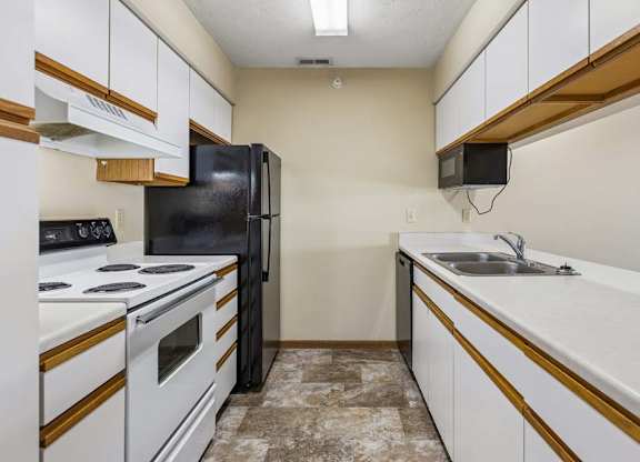 Galley-style apartment kitchen with white cabinets, white oven, black refrigerator, laminate countertops, a double-basin sink, and durable flooring in a functional layout.