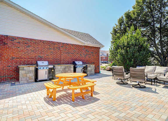 A round picnic table on a patio in front of two grilling stations.