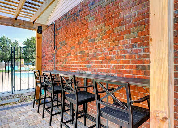 A row of chairs lined up on a patio to a built-in bar top counter..