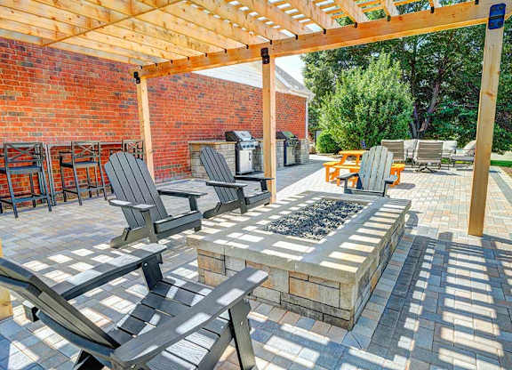 A patio with a pergola covering a fire pit with surrounding chairs.