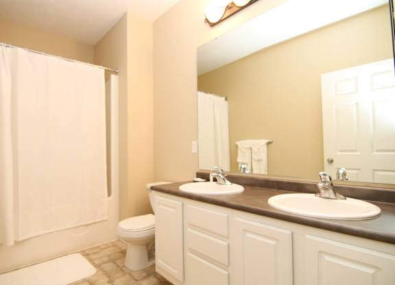 A bathroom with a double sink vanity and tub shower.