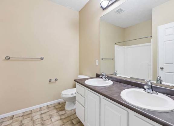 Apartment bathroom with double-sink vanity, large mirror, white cabinetry, and tub shower combo.