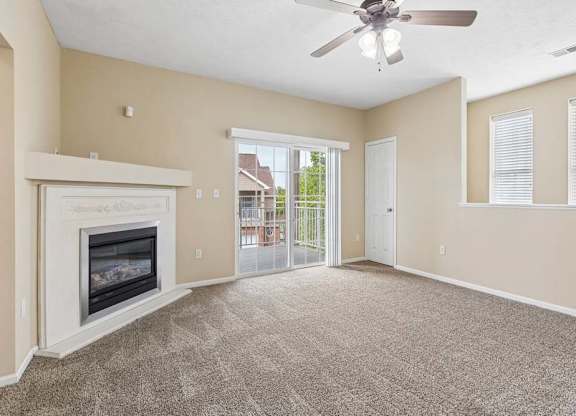 Carpeted apartment living room with fireplace, ceiling fan, sliding glass doors, and private balcony access.