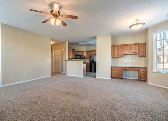 A spacious living room with a ceiling fan and carpeted floor.