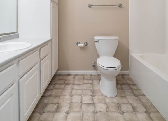 A white toilet sits in a bathroom with a white sink and a white bathtub.