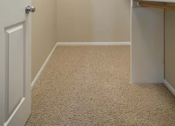 A white door is on the left of a hallway with a carpeted floor.