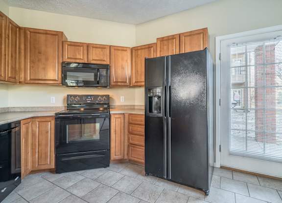 A kitchen with warm cabinetry, black appliances, and a door to a patio space.
