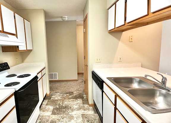 Galley style kitchen with white cabinets and oak trim, white appliances, and tan vinyl flooring
