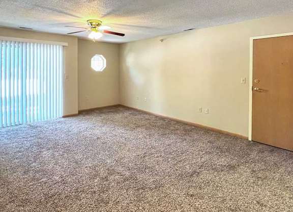 a living room with a ceiling fan, carpeted floor, a sliding glass door with vertical blinds