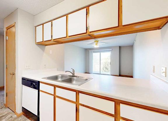 Open kitchen counter with double sink and upper cabinets, connecting to the apartment living area.