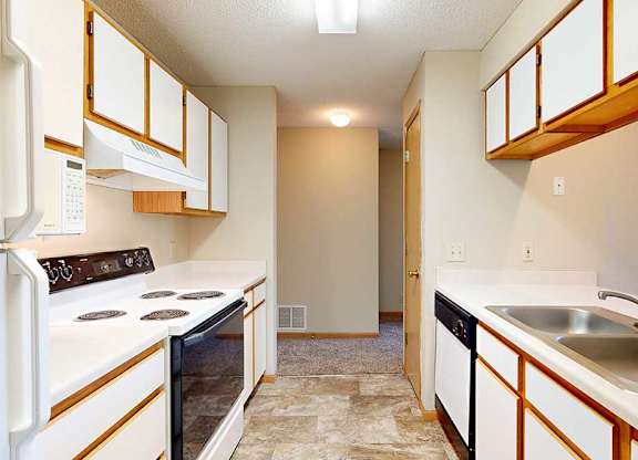 Galley kitchen with white appliances, electric stove, range hood, and wood-trim cabinetry.