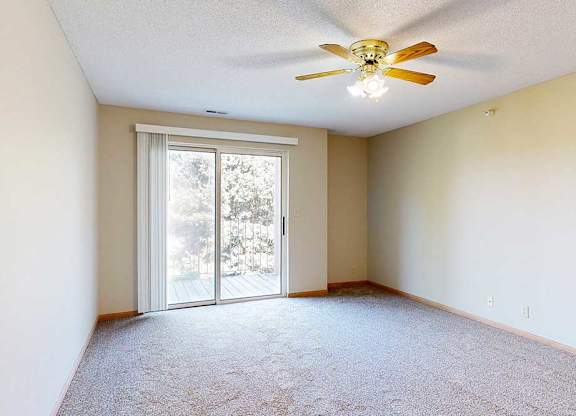 Spacious living room with sliding glass door to balcony, neutral walls, and ceiling fan with light.