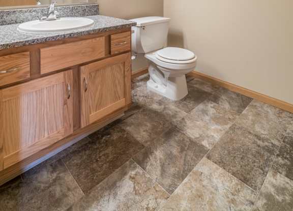A bathroom with a toilet, sink, and wooden cabinets.
