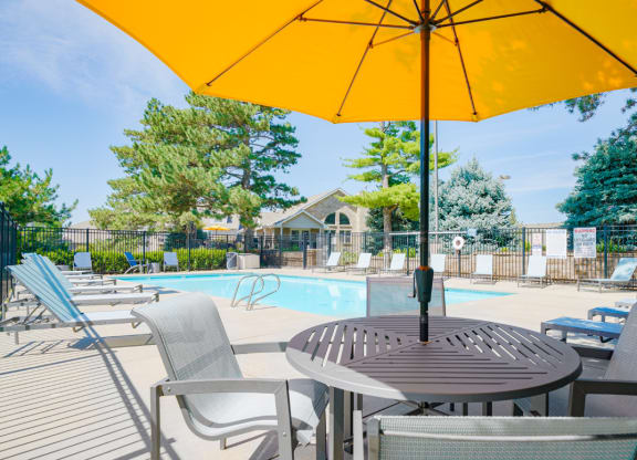 outdoor dining table and chairs shaded with a yellow umbrella next to the swimming pool