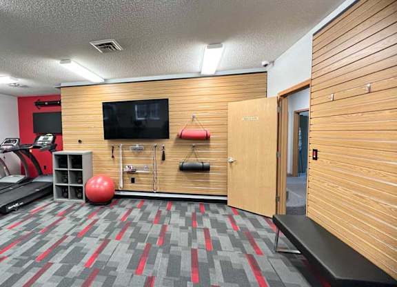 a 24-hour fitness center with treadmills, TVs, yoga equipment, and wooden paneling on the walls