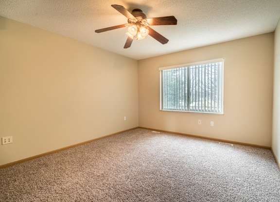 A room with a ceiling fan and a window with blinds.