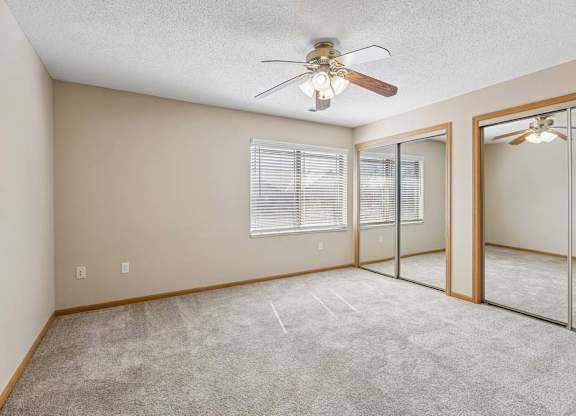 Spacious bedroom with mirrored closet doors, carpet flooring, and ceiling fan.
