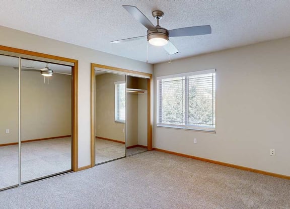 a bedroom with mirrored closet doors , a ceiling fan, and a large window
