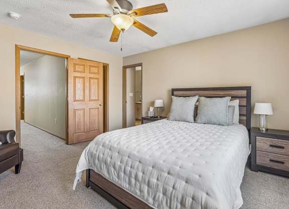 A bedroom with a large bed, a ceiling fan, and a nightstand with a lamp.