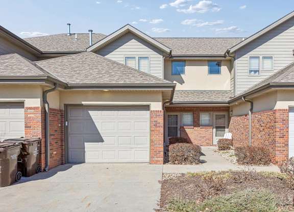 Townhome-style apartment exterior with attached garage, brick accents, and private driveway.