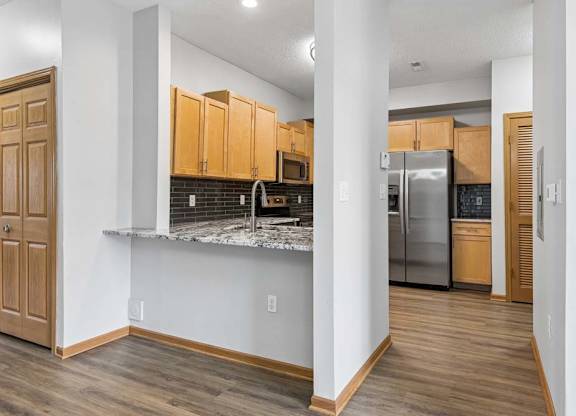 Modern apartment kitchen featuring granite countertops and stainless steel refrigerator.