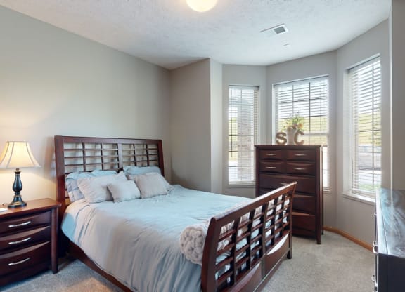 a bedroom with a bed and a dresser brightened with natural light from windows