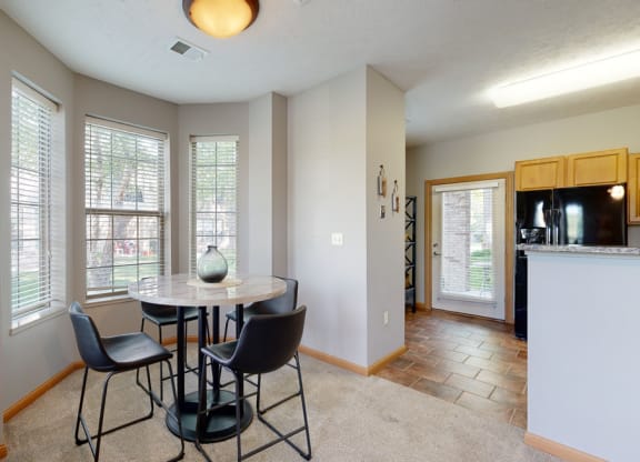 a dining area with a table and chairs and a kitchen in the background