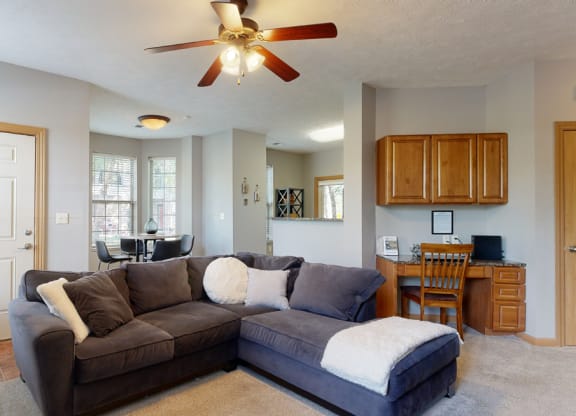a living room with a large sectional couch and a ceiling fan with built in desk in back