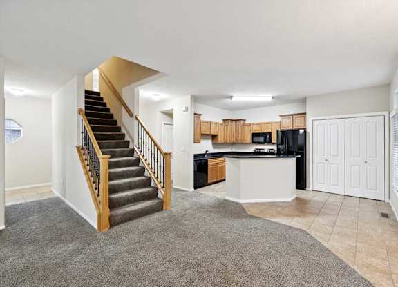 Open-concept living space with staircase, carpet and tile flooring, and kitchen with peninsula seating.