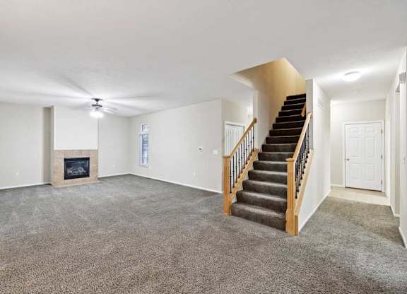 Open living space featuring staircase, fireplace, and wide carpeted area for flexible furniture layout.
