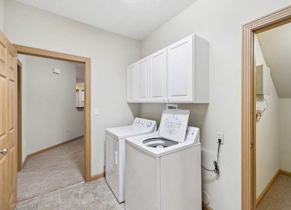 Laundry area with overhead cabinetry, adjacent utility closet, and doorway to carpeted living space.