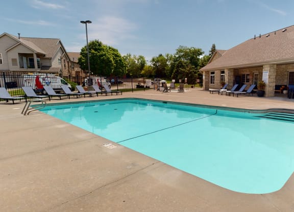a swimming pool with lounge chairs and the clubhouse building in the background
