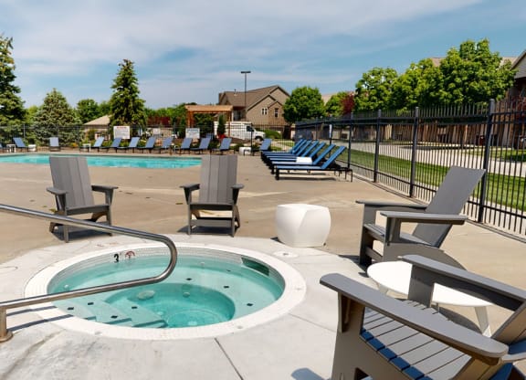 a hot tub with chairs around it and pool and trees in the background